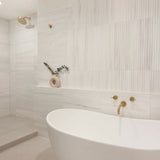 Modern bathroom with a freestanding bathtub, gold fixtures, and decorative elements.